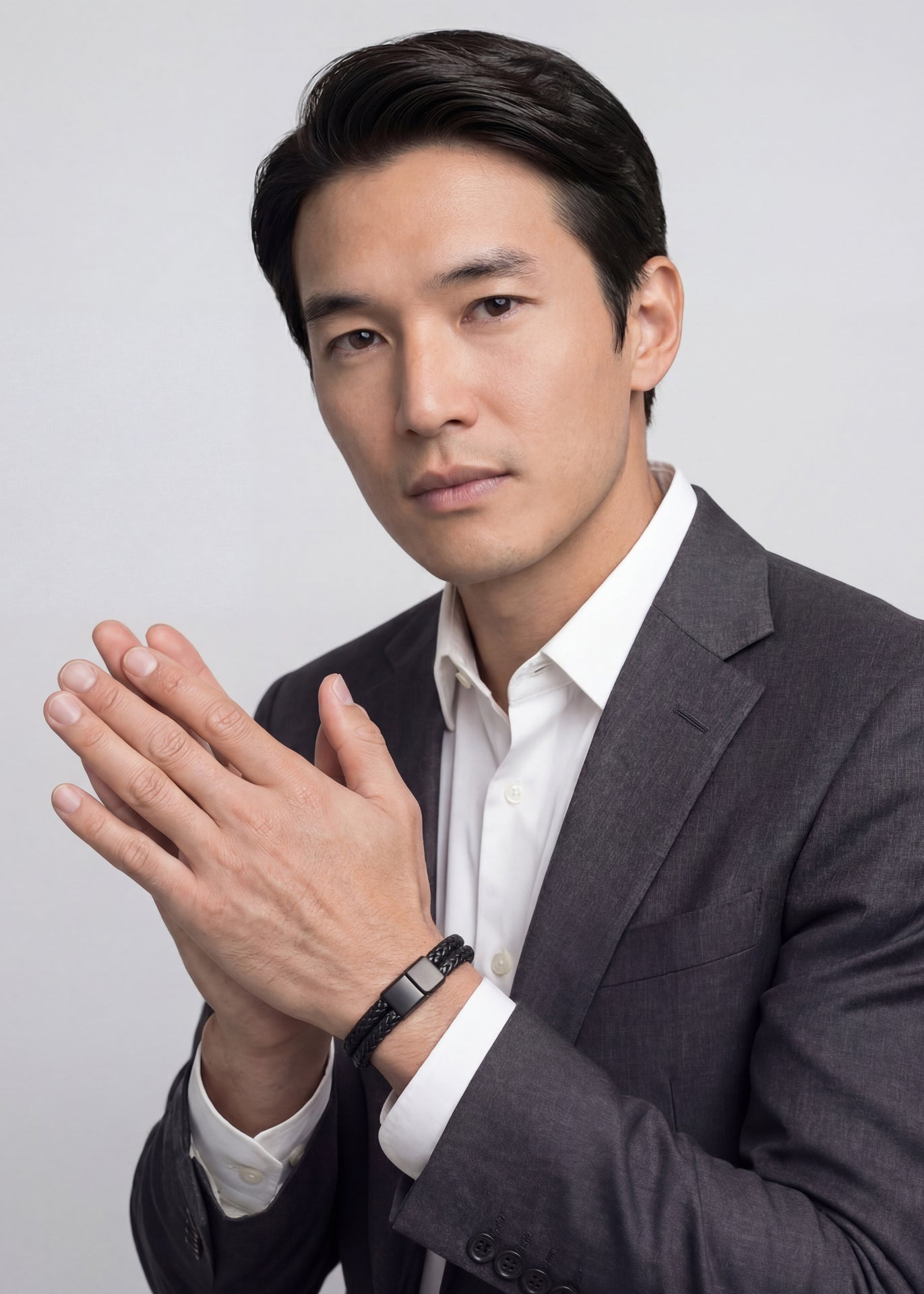 Man in a suit with hands clasped together against a plain background