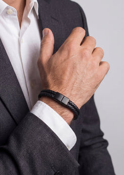 Person wearing a black braided bracelet on a plain background