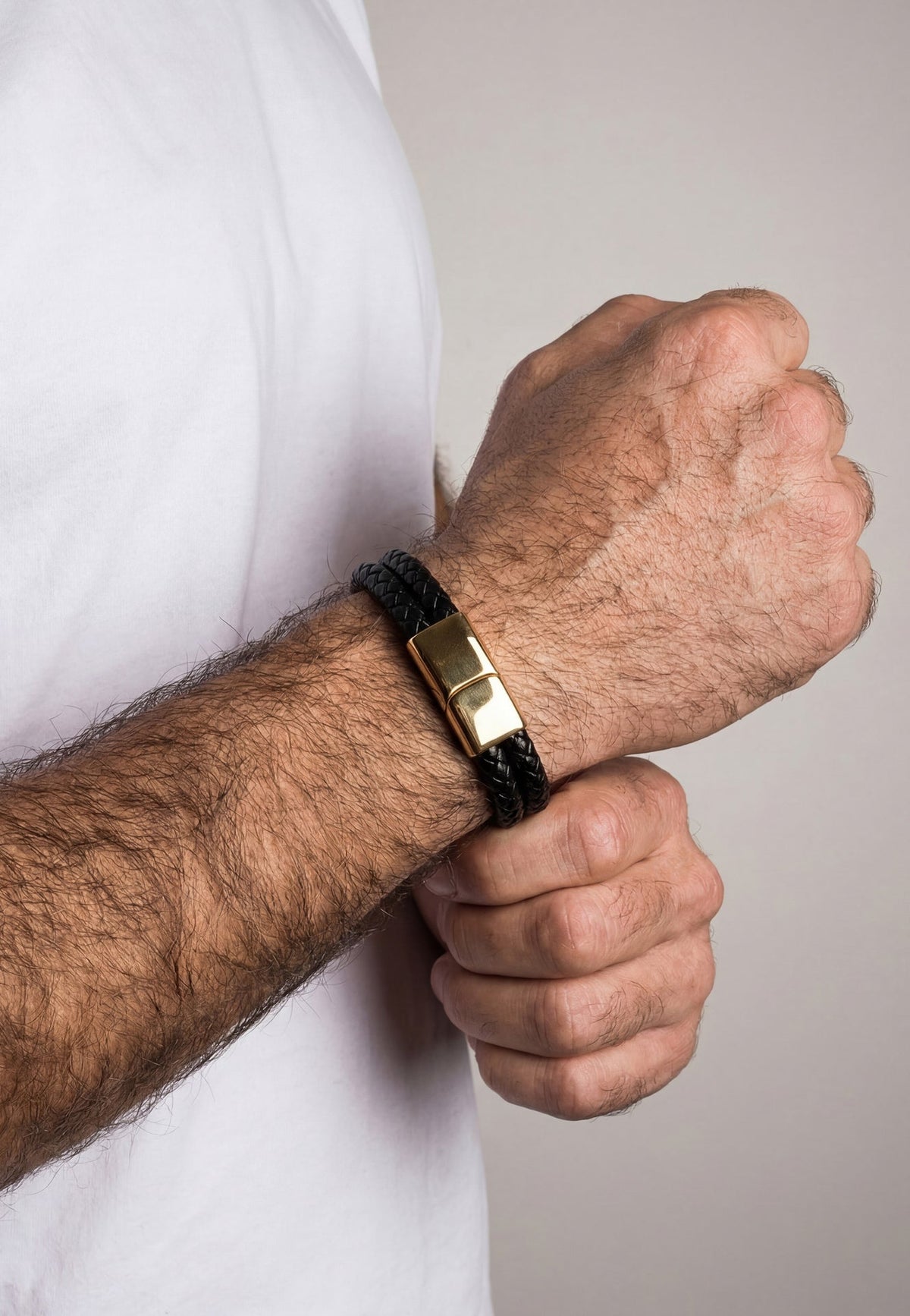 Person wearing a black bracelet with a gold clasp on a neutral background