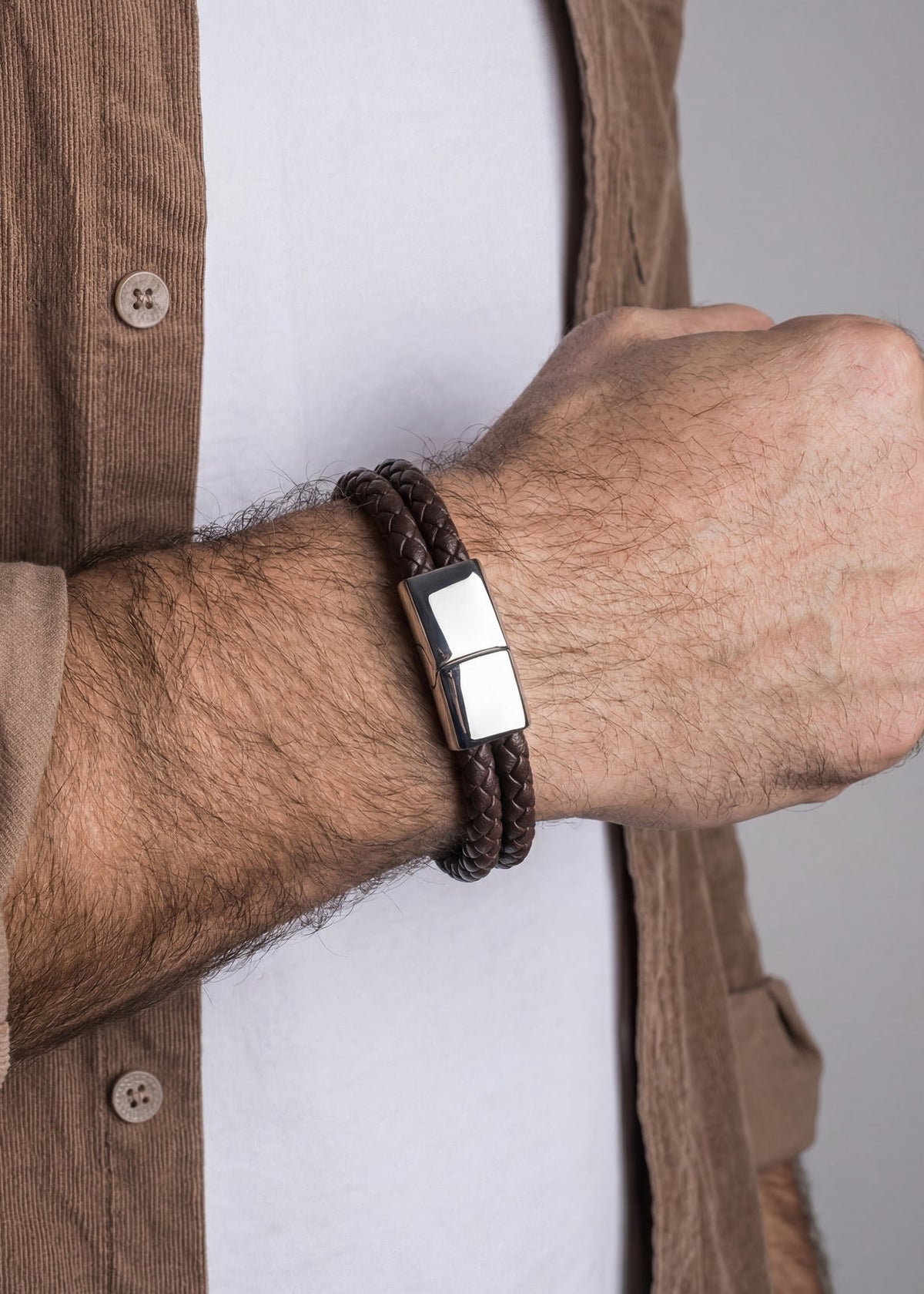 Brown braided bracelet with a silver magnetic clasp on a wrist, against a neutral background.
