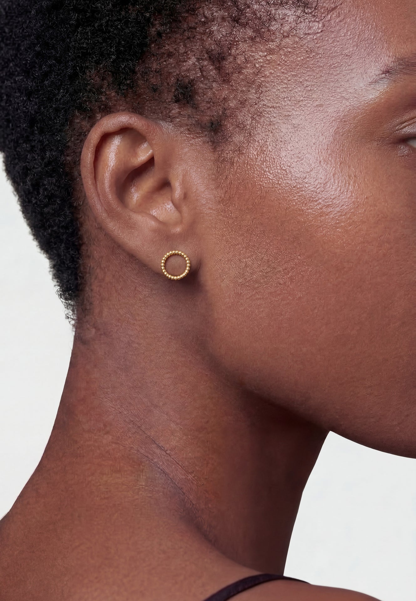 Close-up of a person wearing gold hoop earrings on a neutral background