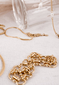 Gold jewelry including a bracelet and earrings on a light fabric background
