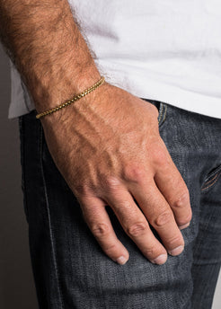 Hand wearing a gold bracelet with a plain background